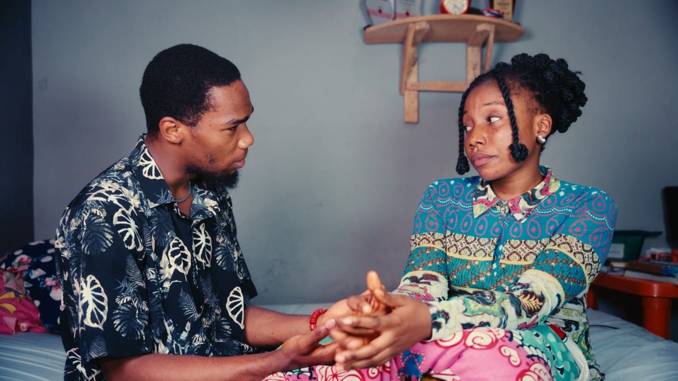 A man and a lady facing each other while sitting on a bed